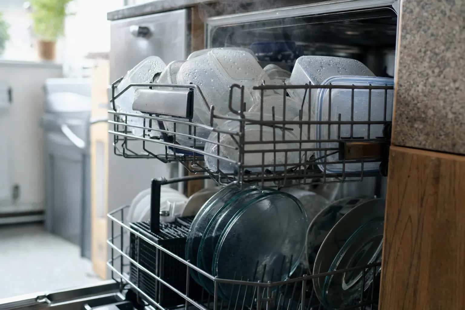 An open dishwasher with racks of glasses and plates still wet after a cycle