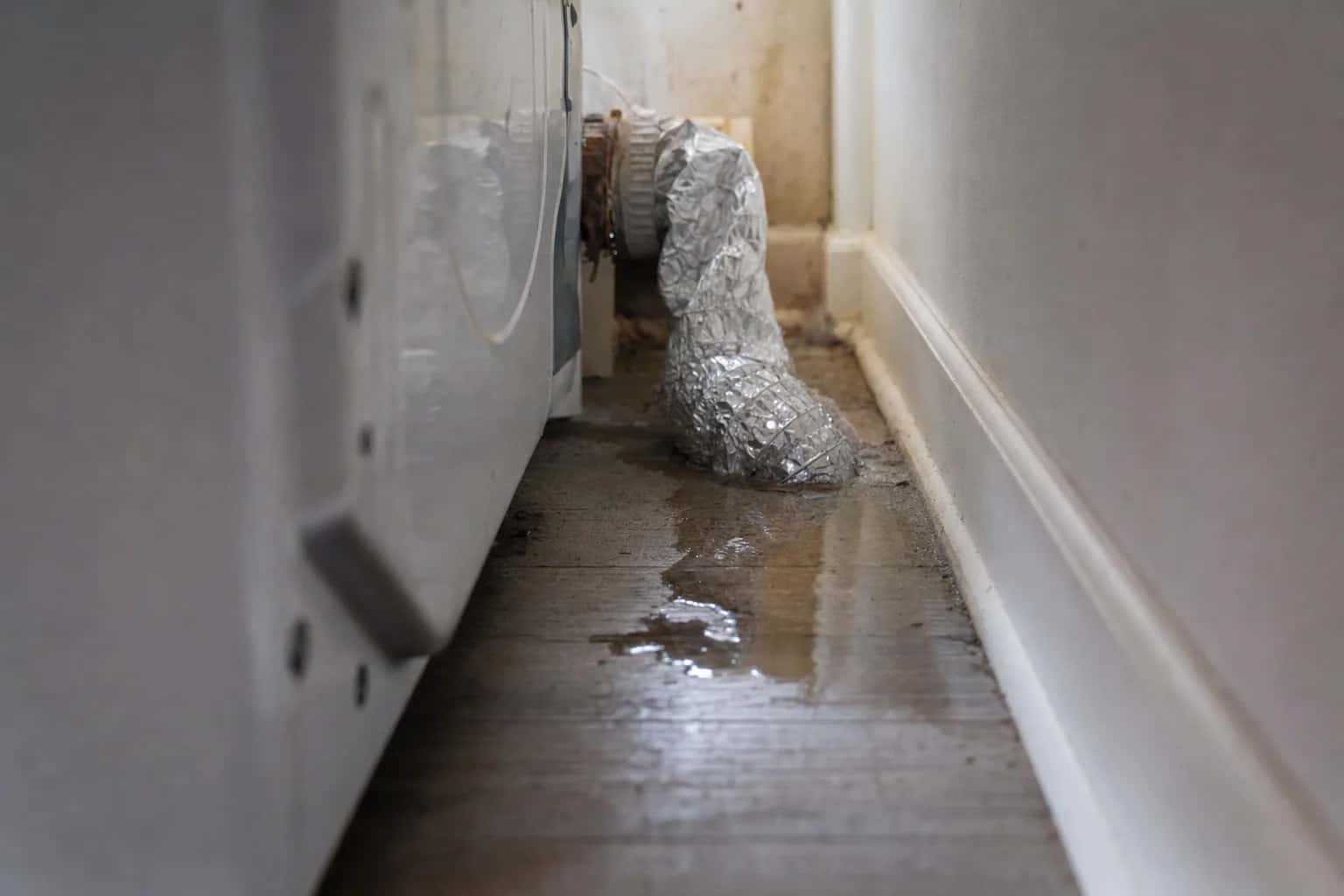 Water on the floor beside a dryer, with a foil vent hose behind it