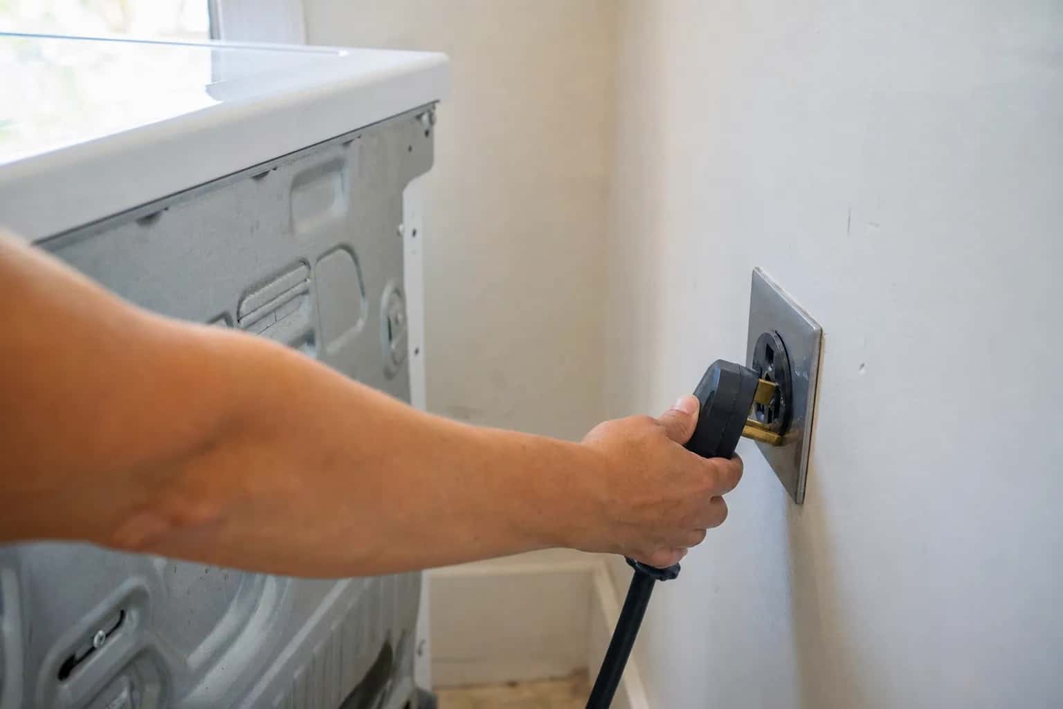 A hand pressing a dryer plug into a 240-volt wall outlet