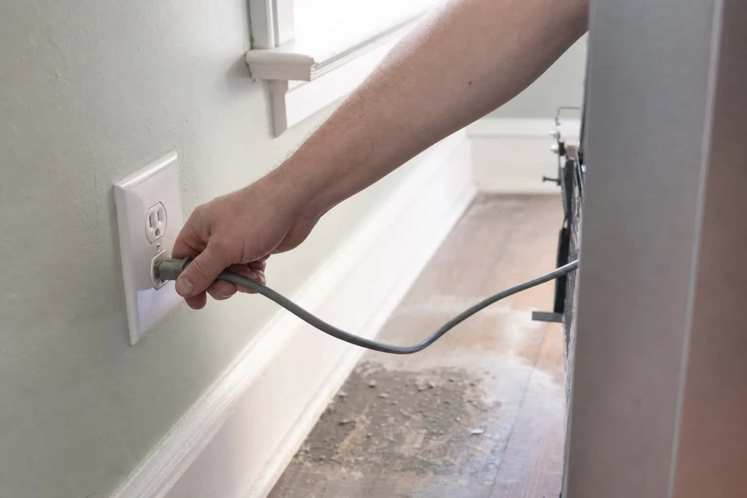 A hand unplugging a refrigerator power cord from a wall outlet
