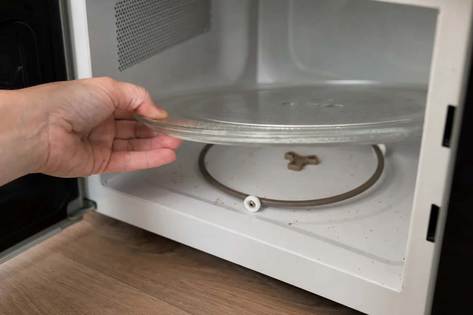 A hand lifting the glass turntable out of a microwave