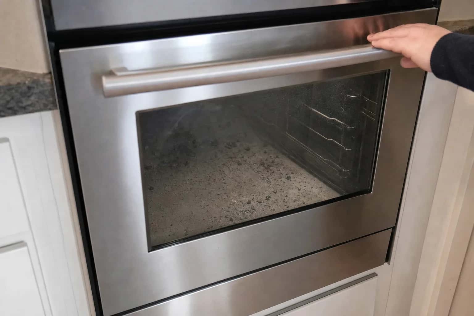 A hand pulling the handle of a locked oven door