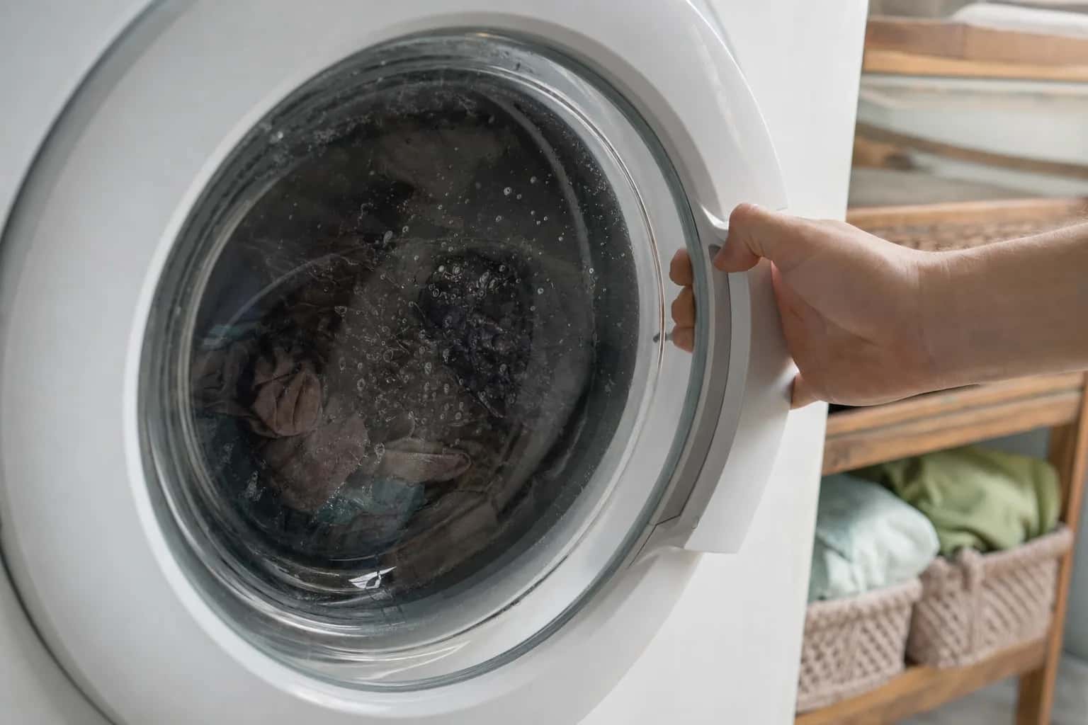 A hand pulling the door handle of a front-load washer with water inside