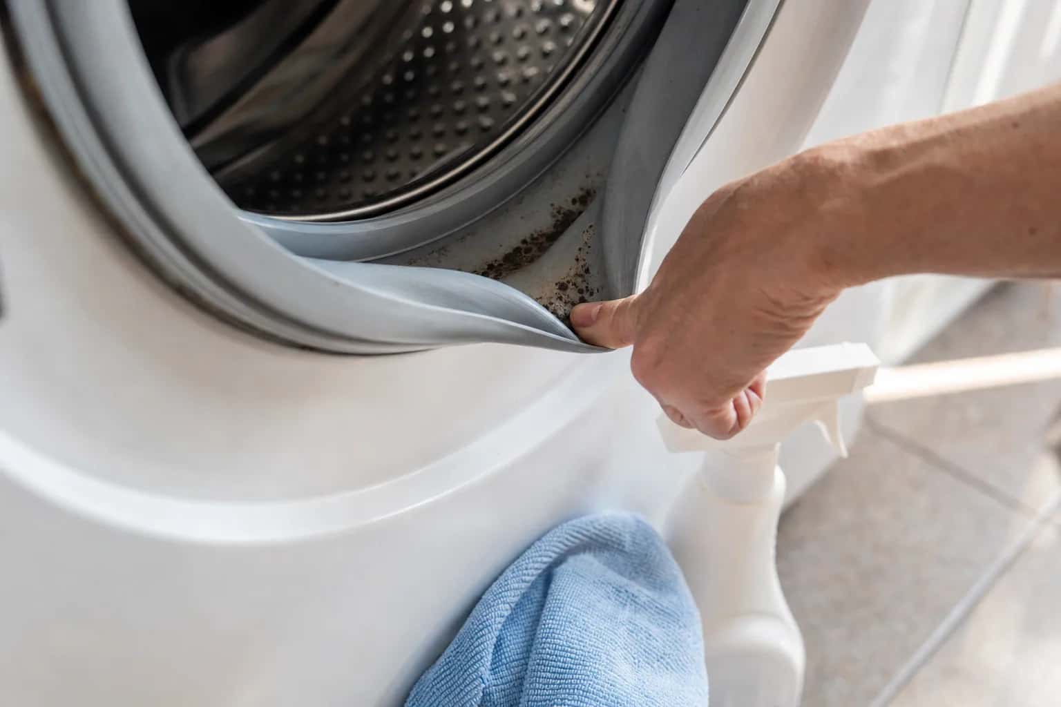 A hand pulling back the rubber door gasket of a front-load washer