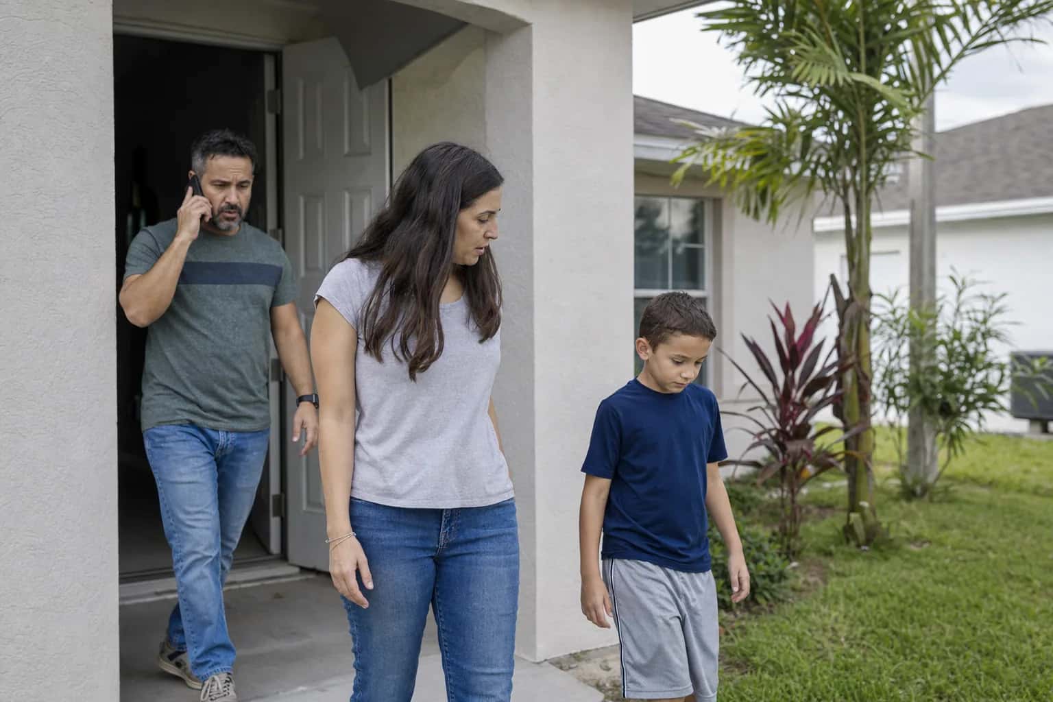 A family walking out of their front door into the yard, one adult on the phone